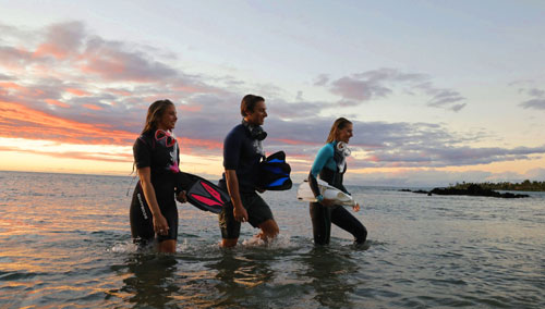 Three young snorkelers wading in water at sunset