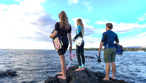 Three young snorkelers standing on a rock by the ocean