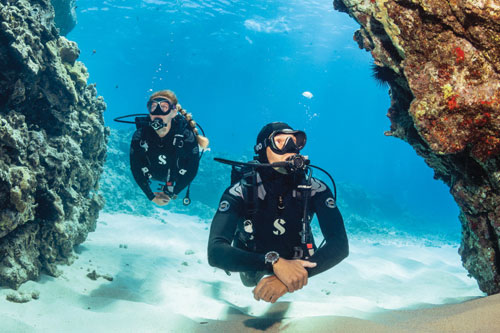 Divers underwater swimming between coral reefs