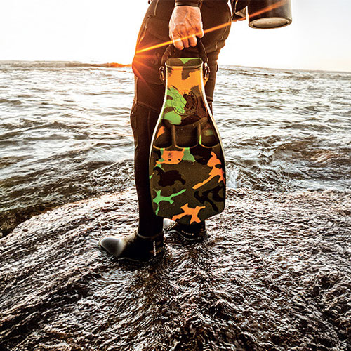 Diver standing in the surf carrying camo Jet Fins