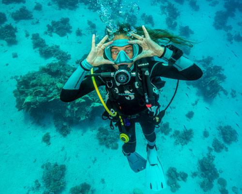 Underwater diver in aqua colored water looking up at the camera