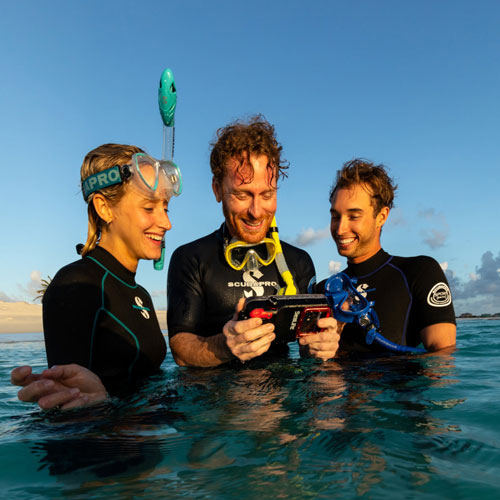 Three snorkelers in SCUBAPRO divewear standing in shallow ocean water