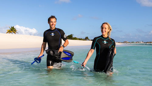 Two snorklers walking into the ocean from the beach